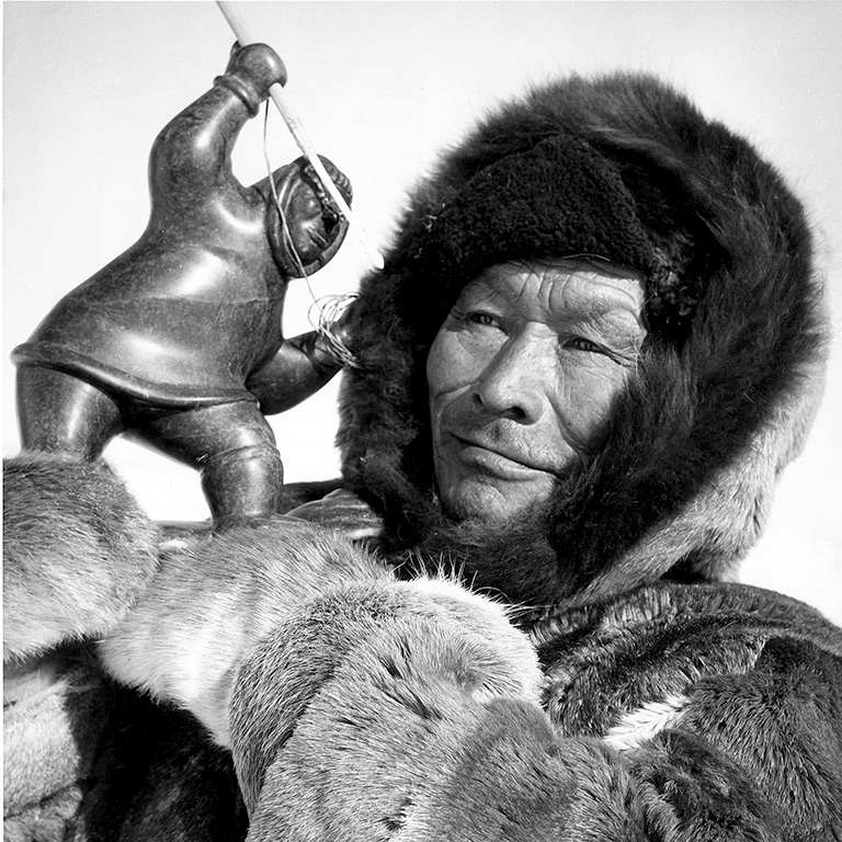 Une photo en gros plan d'un homme en parka tenant une sculpture inuite.