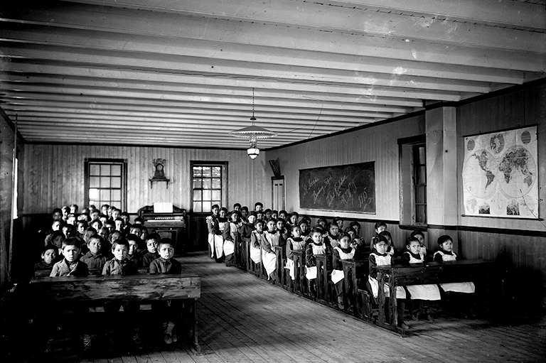 Une photo en noir et blanc d'élèves en uniformes scolaires assis derrière un bureau.