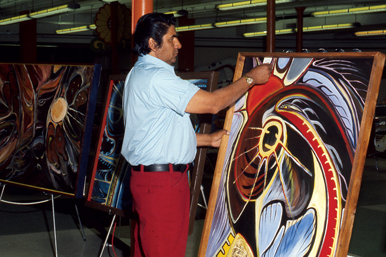 A man in red pants holds a large painting in a frame.