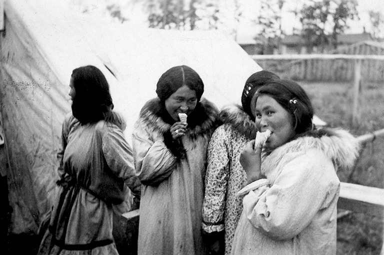 Photo en noir et blanc de quatre femmes en parkas. Deux mangent de la crème glacée et regardent vers la caméra.