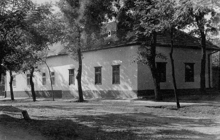 Photo en noir et blanc d’une grande maison rectangulaire entouré d’arbres.