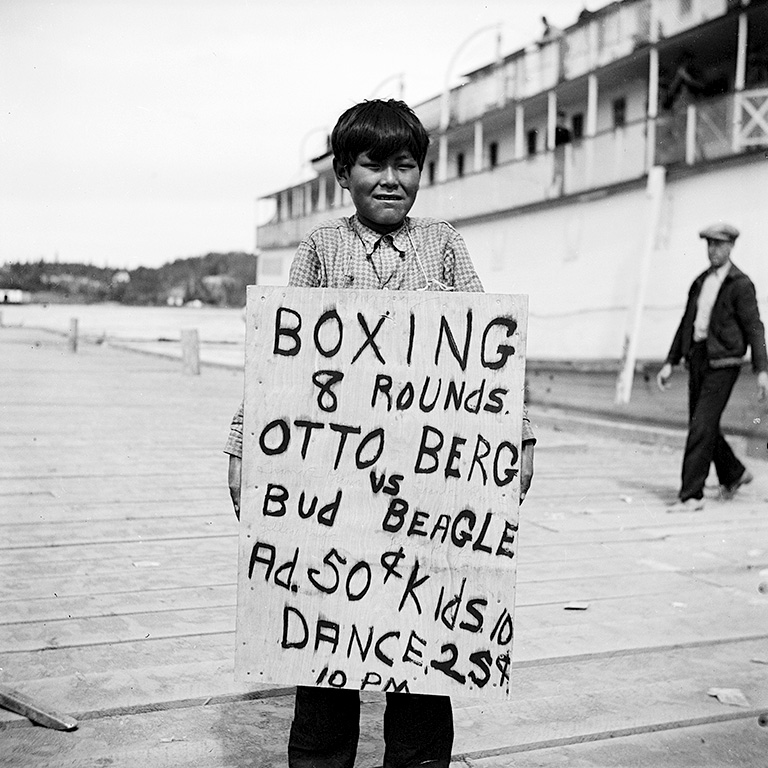 Un garçon tient une pancarte annonçant un match de boxe en huit rounds.