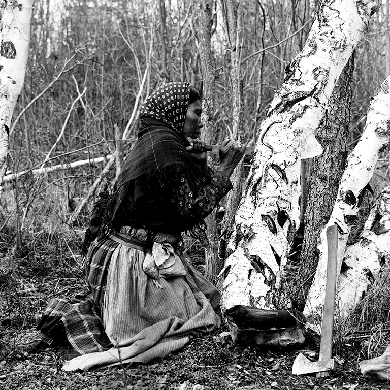 Photo en noir et blanc d'une femme agenouillée à côté d'un arbre et creusant dedans.