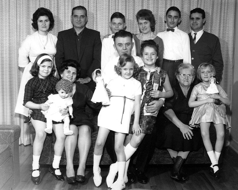 Photo en noir et blanc d’un groupe de personnes composé d’hommes, de femmes et d’enfants. Six sont debout à l’arrière, les autres sont assis devant. L’homme au centre tient deux enfants sur ses genoux